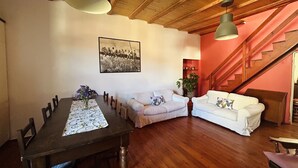 A dining area with a wooden table, chairs, and a vase of flowers. There is a white sofa and a staircase in the background. - Tango House (Zandobbio)