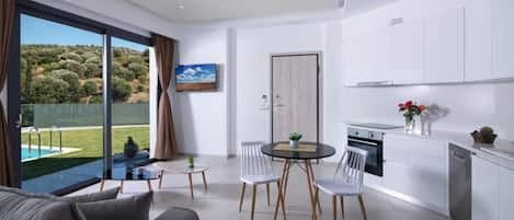 A modern kitchen with white cabinets, a dining area with a round table and chairs, and a large window overlooking a pool and greenery.
