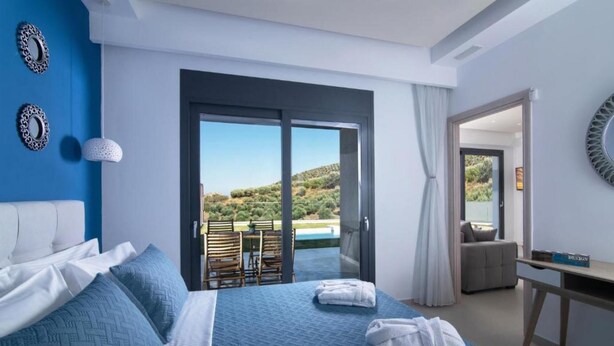 A bedroom with a large bed, a desk, and a view of a pool and hills. - Deluxe Villa Christos (Malevizi)