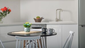 A modern kitchen with white cabinets, a black countertop, a coffee maker, a mug, a vase with flowers, and a small potted plant. - Deluxe Villa Christos (Malevizi)