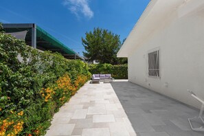An outdoor patio with a white wall, a green awning, a metal gate, and a bench.