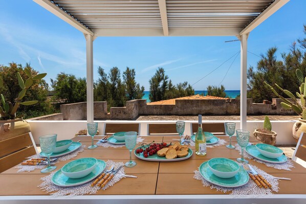 A table set for two with a view of the sea, a pergola, and cacti.