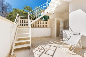 A staircase leading to a balcony, a white chair, and a tiled floor.