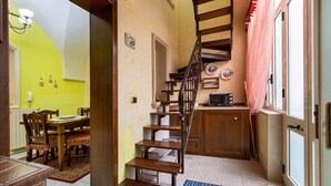 A kitchen with wooden cabinets, a dining area with chairs, a staircase, and a microwave. - 3283 Appartamento Garibaldi by Barbarhouse (Carmiano)