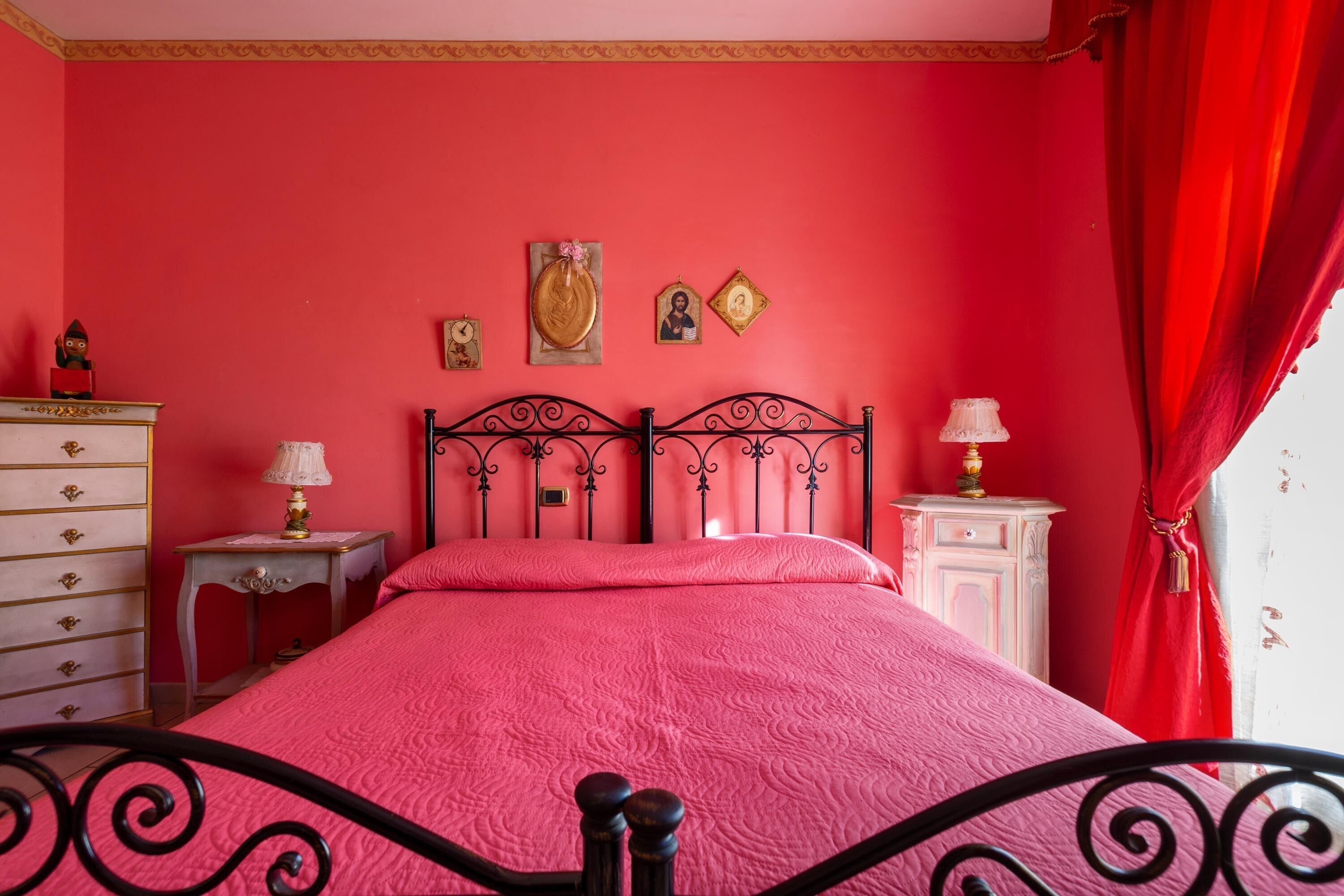A room with a bed, a dresser, a nightstand, and a wall with religious icons.