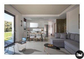 Relax in this spacious living area with a large sofa, dining table, and kitchen in the background.
