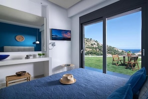 Relax in this serene bedroom with a large bed, flat-screen TV, and sliding glass door leading to a balcony with a hillside view.