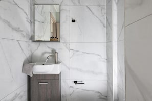 Bathroom features a sink, mirror, and marble-tiled walls with a wooden cabinet below.
