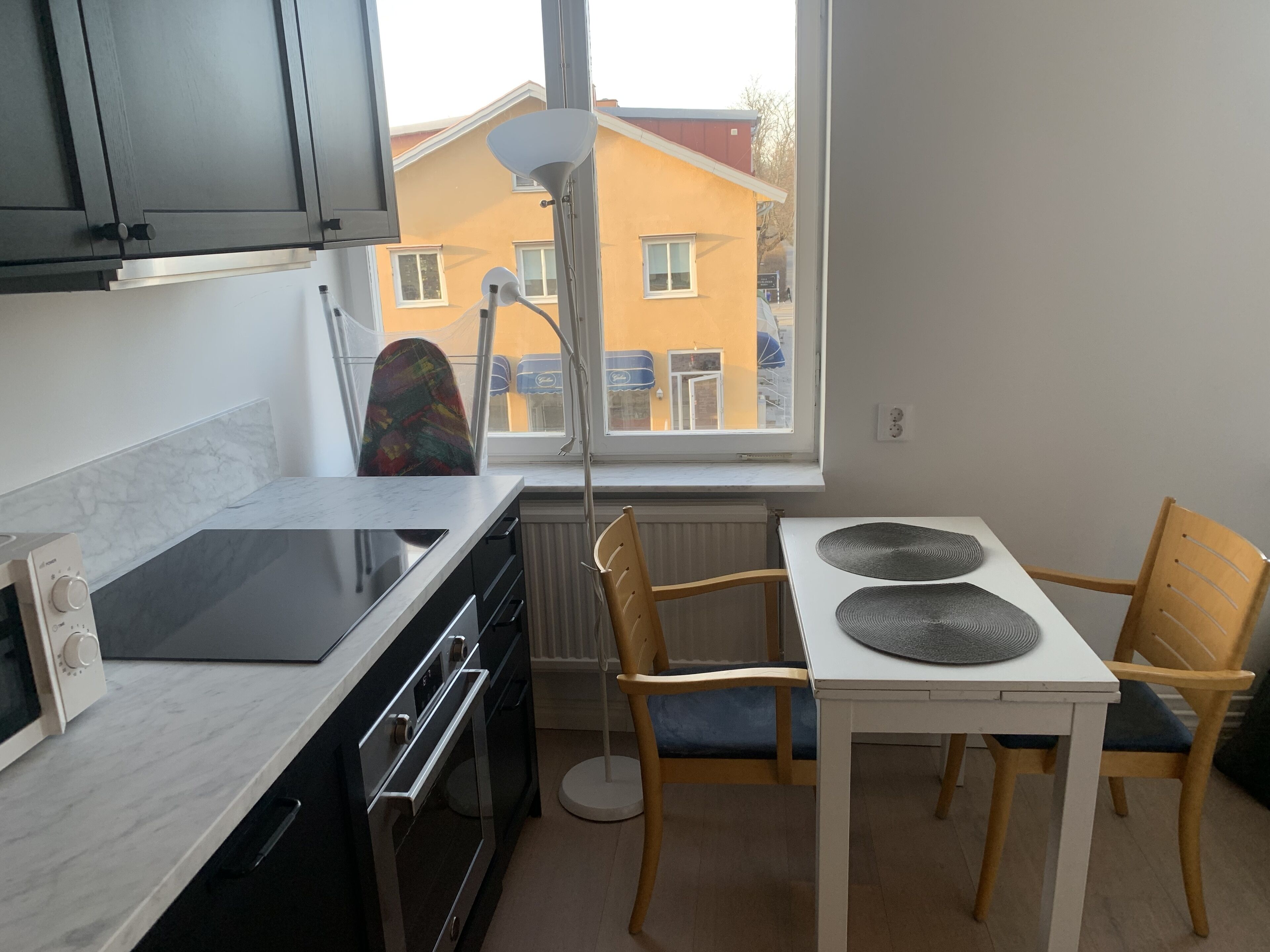 A modern kitchen with a stove, oven, and microwave. There is a dining table with chairs and a window with a view of buildings outside.