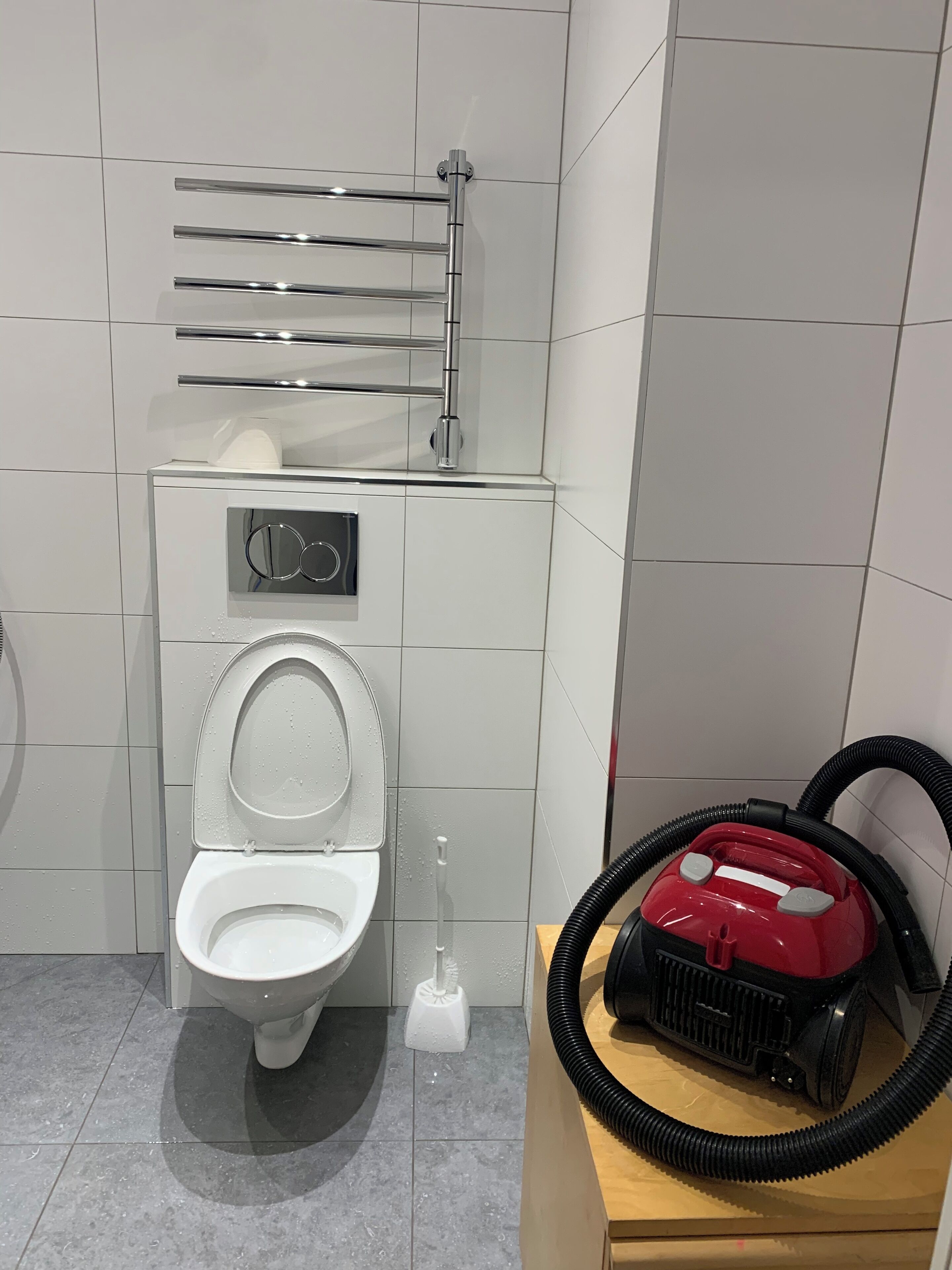 A bathroom with a toilet, a hand dryer, and a vacuum cleaner.