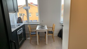 Eine kleine Küche mit Essbereich, ein Fenster mit Blick auf ein gelbes Gebäude und ein Heizkörper unter dem Fenster.