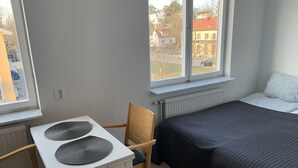 Ein Schlafzimmer mit einem Bett, einem Tisch mit zwei Platzsets, einem Stuhl und einem Fenster mit Blick auf Gebäude.