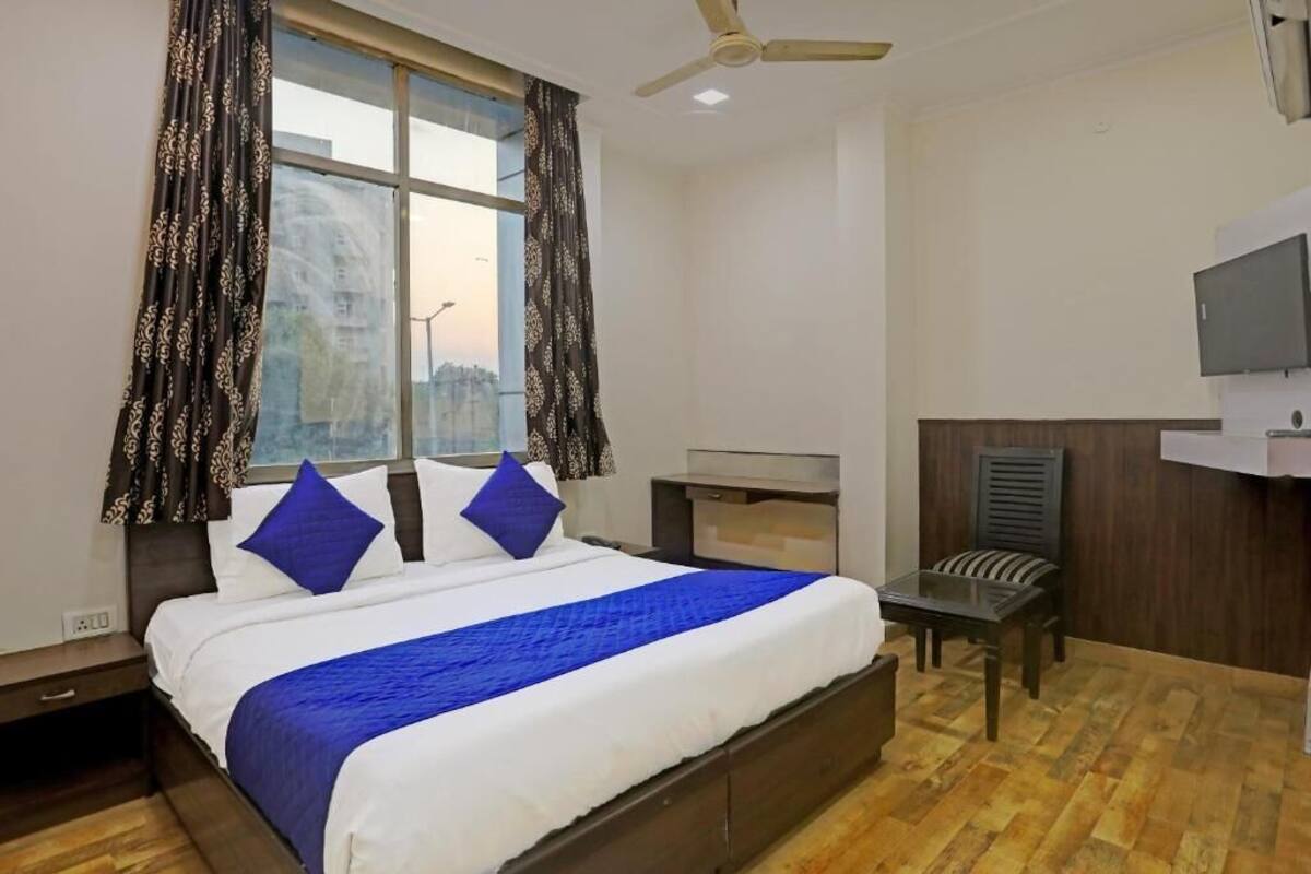 A hotel room with a large bed, a desk, a chair, a television, and a window with curtains.