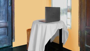 A laptop on a table with a white tablecloth, a wooden chair, and a door with a metal handle. - SPOT ON 92063 Balebat Endah Syariah (Pangandaran)