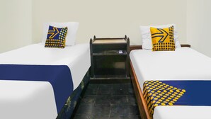 A hotel room with two single beds, each with a white mattress and a blue and yellow pillow. There is a small wooden bench between the beds. - SPOT ON 92063 Balebat Endah Syariah (Pangandaran)