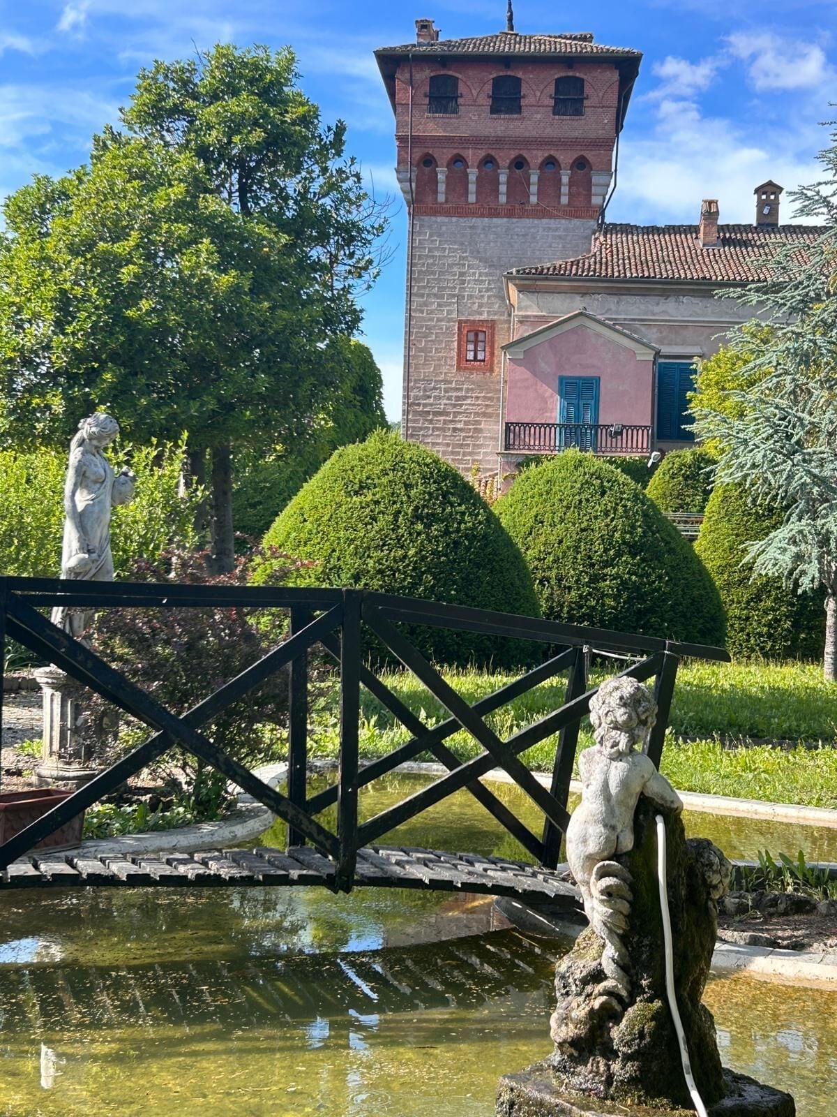 Un jardín con un estanque, estatuas y un edificio con una torre.