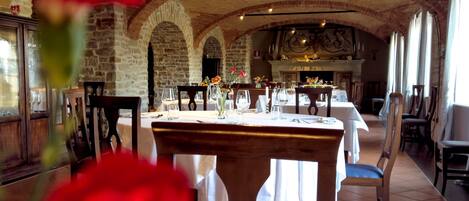 A restaurant with brick arches, tables set for dining, and a fireplace.