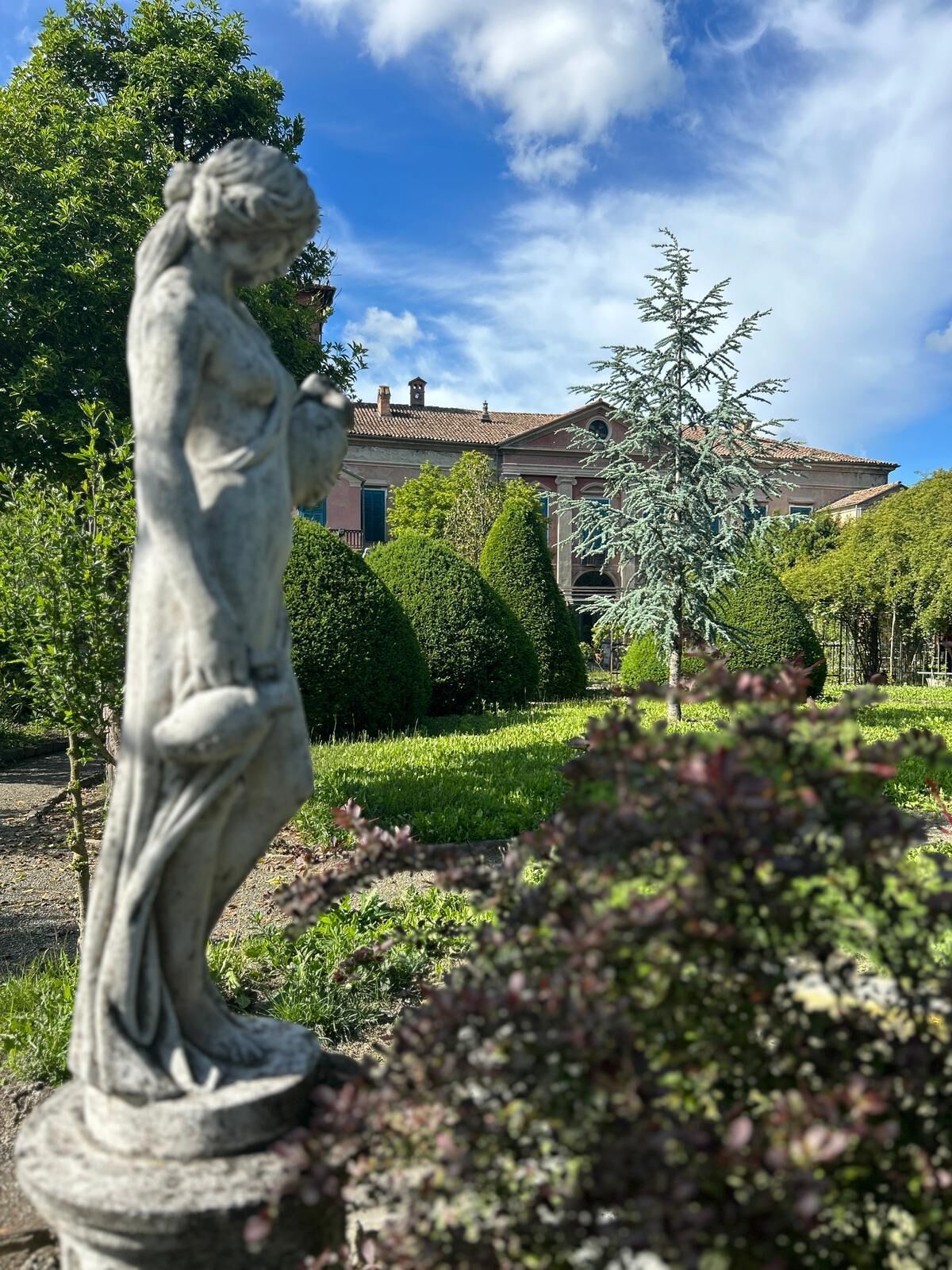 Una estatua en un jardín, con un edificio al fondo.