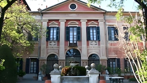 A classical building with a central arched window, flanked by columns, and a fountain in the foreground. - Il Castello di Bubbio (Bubbio)