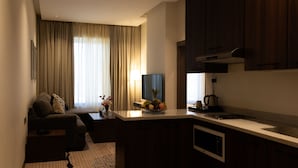 A modern living room with a sofa, a coffee table, and a TV. There is a kitchen area with a microwave and a fruit bowl. - Dream Residence (Al Khobar)