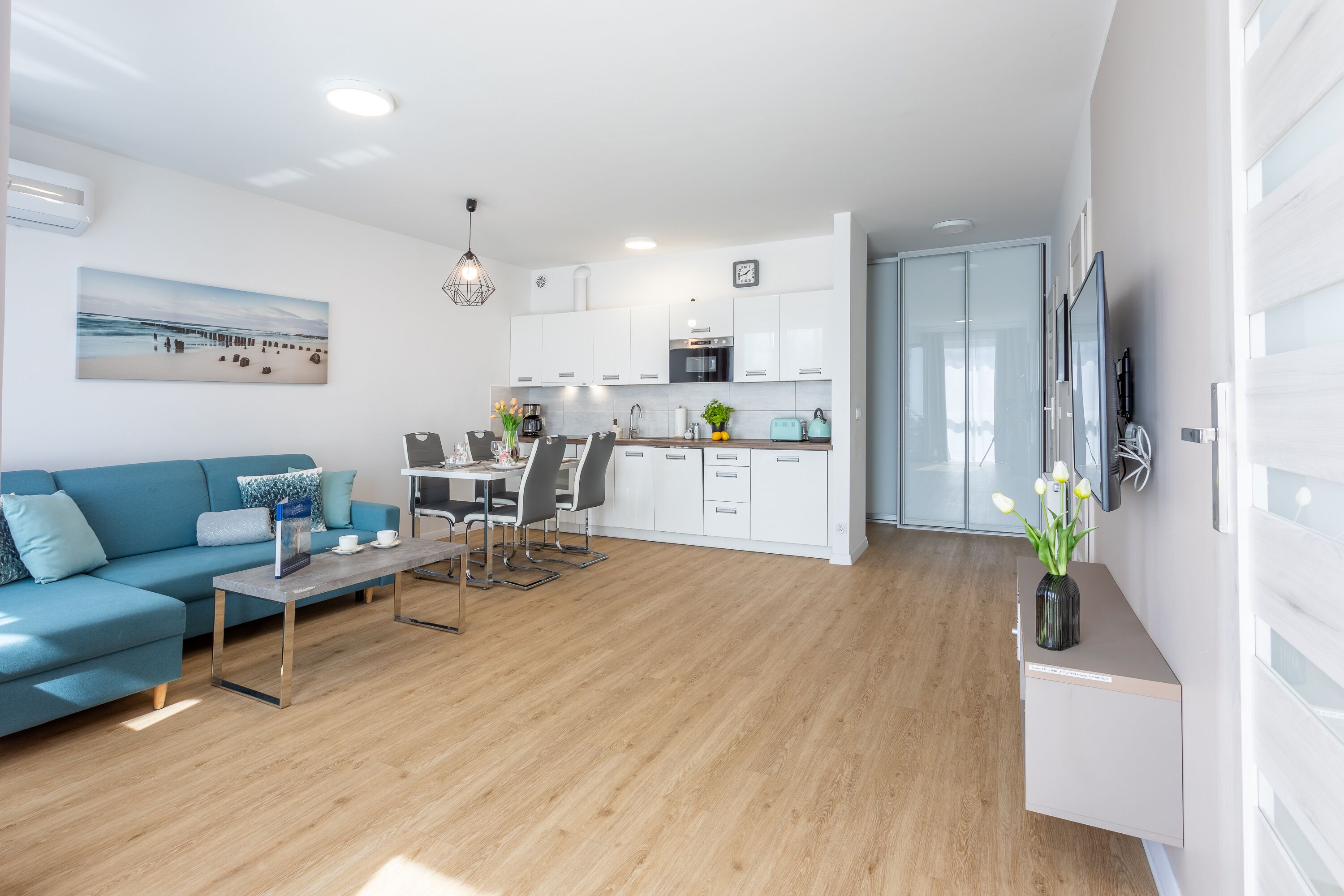Una sala moderna con un sofá azul, una mesa de comedor con sillas y una zona de cocina con armarios blancos y un microondas.