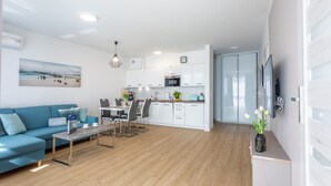 Una sala moderna con un sofá azul, una mesa de comedor con sillas y una zona de cocina con armarios blancos y un microondas.