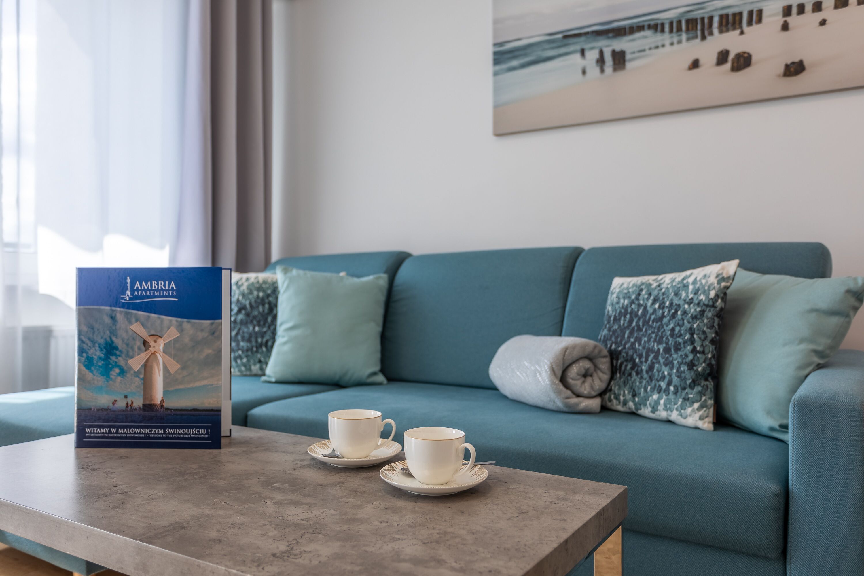 A room with a teal sofa, two white cups on a table, and a brochure on the table.