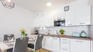 Cocina moderna con armarios blancos, encimera de madera y comedor con dos sillas y una mesa preparada para dos.