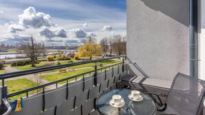 Un balcón con mesa y sillas, con vistas a un parque y un río.