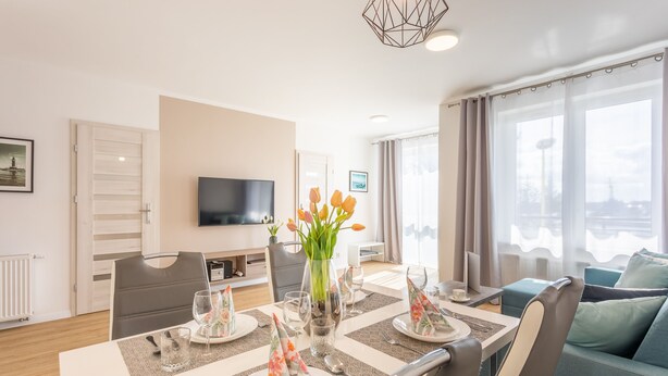 Una sala de estar moderna con comedor, televisor de pantalla plana y un amplio ventanal con cortinas.