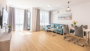 Una sala de estar moderna con sofá, mesa de comedor y sillas, televisor de pantalla plana y un ventanal con cortinas.