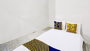 Una habitación pequeña y limpia con una cama, dos almohadas y suelo de baldosas.