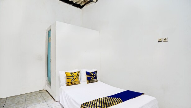 Una habitación pequeña y sencilla con una cama individual, dos almohadas y una manta azul y amarilla.