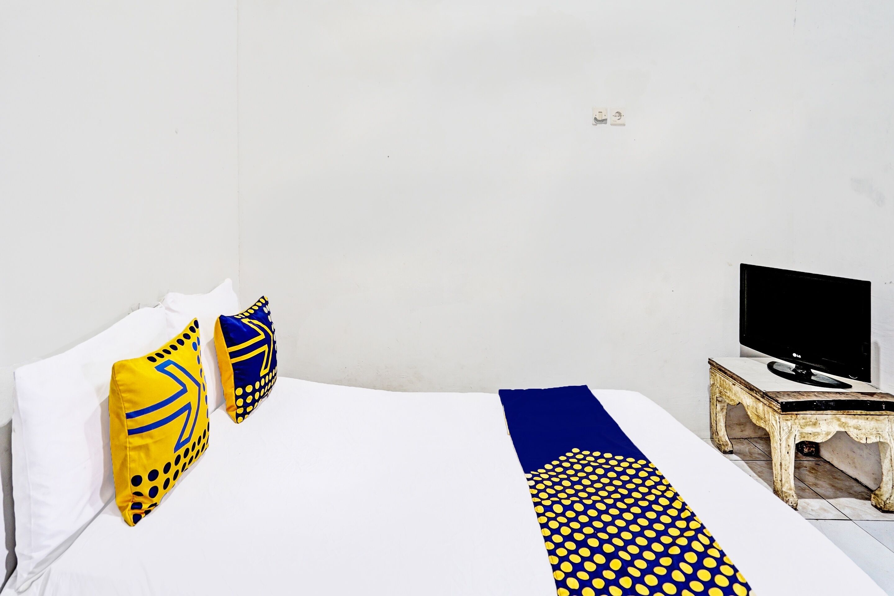 A bedroom with a bed, two pillows, a blanket, a television on a small table, and a white wall.