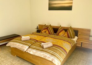 A neatly made bed with a patterned bedspread and pillows, a bedside table with a lamp, and a wall-mounted picture.