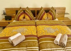 Una cama bien hecha con una colcha estampada y almohadas, una mesita de noche con un teléfono y un pequeño dispositivo electrónico.