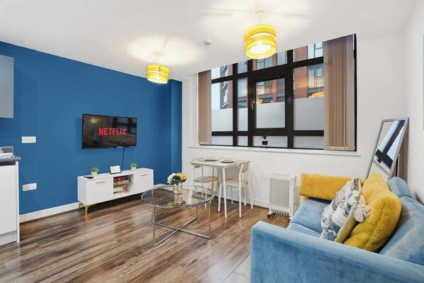 Ein modernes Wohnzimmer mit blauer Wand, einem Flachbildfernseher, einem Couchtisch, einer Couch und einem Essbereich.