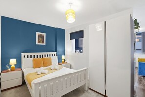 Ein Schlafzimmer mit einem weißen Bett, blauen Wänden, einem weißen Kleiderschrank und einem Fenster mit Blick.