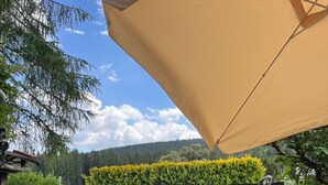Une terrasse extérieure avec une table et des chaises, un grand parasol et une vue sur une zone boisée.