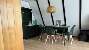 Un espace de salle à manger moderne avec une table et des chaises vertes, un luminaire suspendu et une cuisine en arrière-plan.