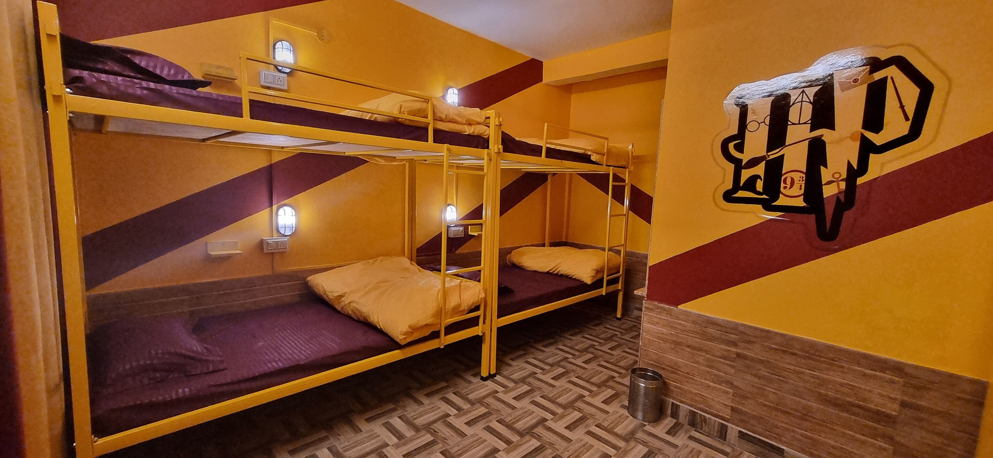 A dormitory room with bunk beds, a wooden herringbone floor, and a wall with a geometric pattern.