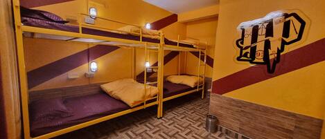 A dormitory room with bunk beds, a wooden herringbone floor, and a wall with a geometric pattern.