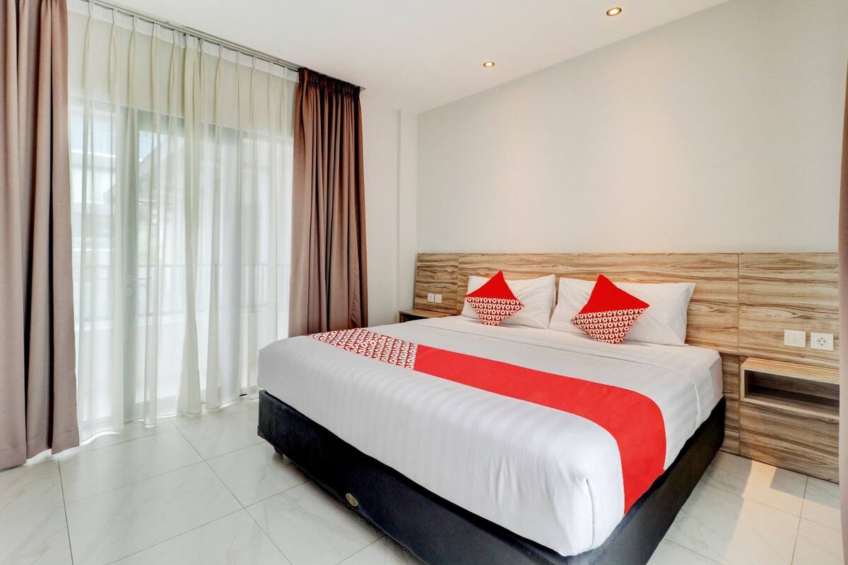 Een hotelkamer met een groot bed, een houten hoofdbord, een nachtkastje en een raam met gordijnen.