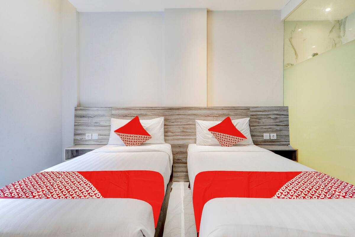 Een hotelkamer met twee bedden, elk voorzien van een rood-wit gebekeerd beddegoed en passende kussens. De kamer heeft een modern design, met een marmeren accentmuur en een houten hoofdbord.