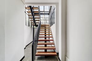 Un escalier moderne avec des marches en bois et des rampes noires, menant à une pièce dotée de grandes fenêtres.
