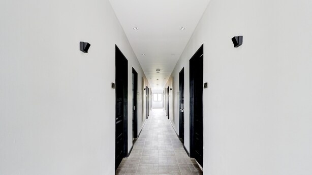 A long, narrow hallway with white walls and black doors, leading to a bright end. - Collection O Cihampelas Near Ciwalk Formerly I Sleep Hotel (Bandung)