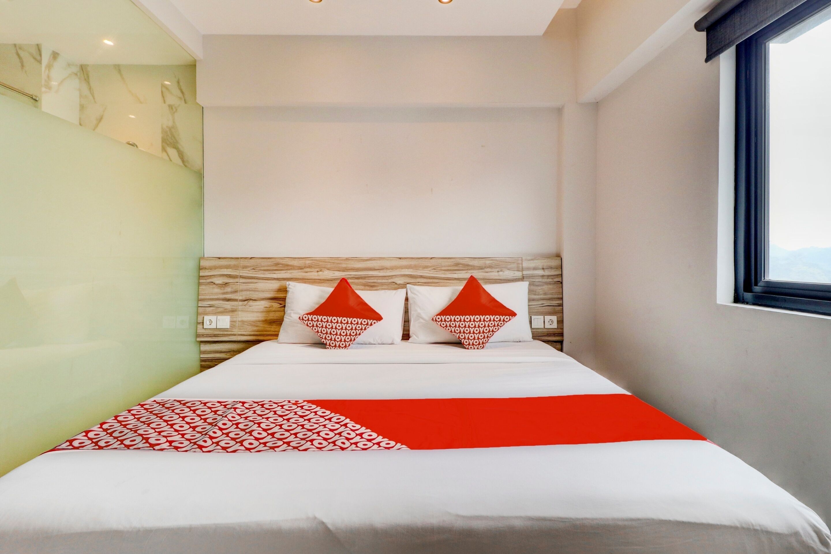 Une chambre d’hôtel moderne avec un grand lit, deux oreillers rouges, une tête de lit en bois et une vue sur les montagnes par la fenêtre.