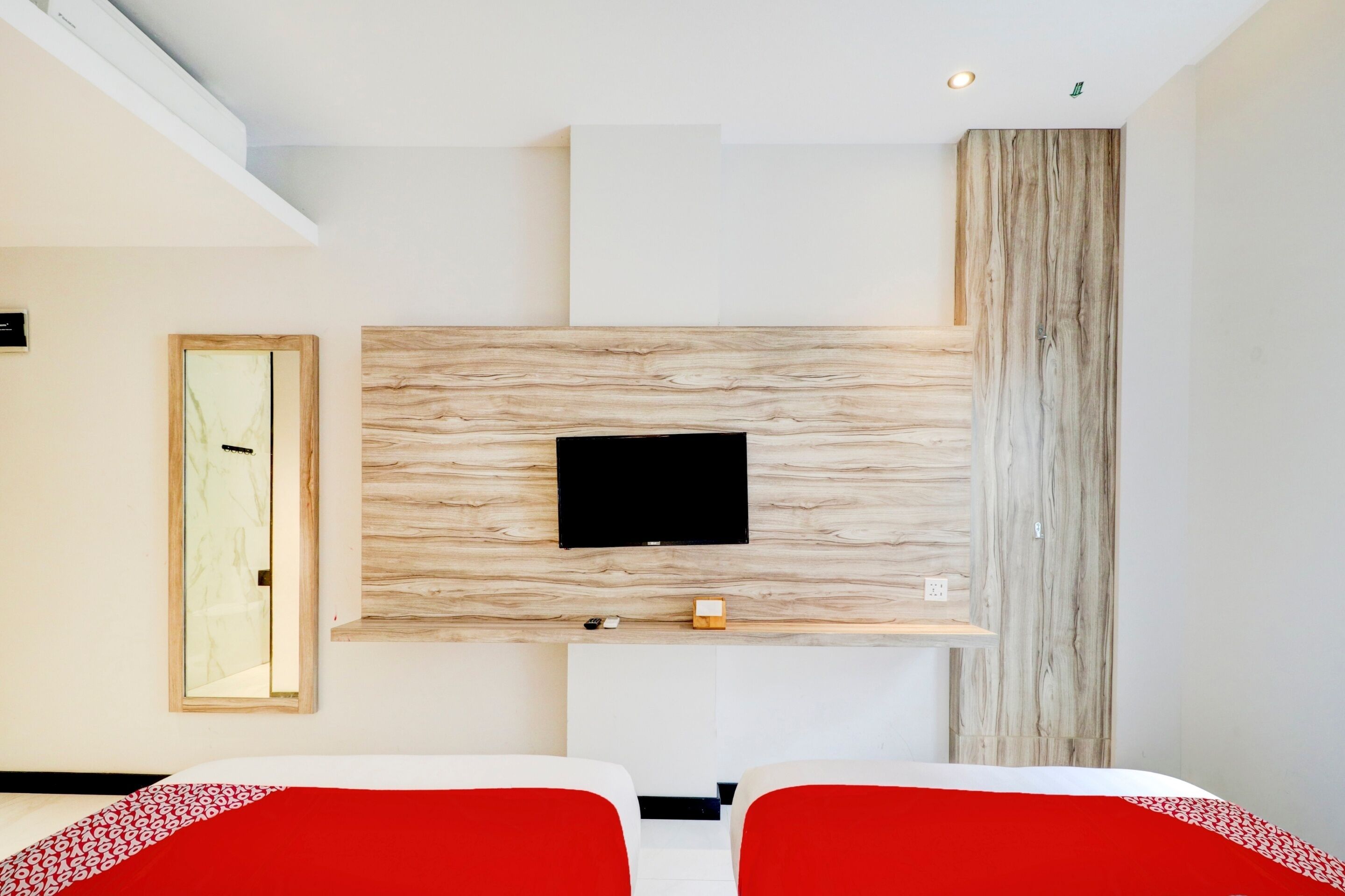 A modern hotel room with a mounted TV, a wooden accent wall, and a red bedspread.