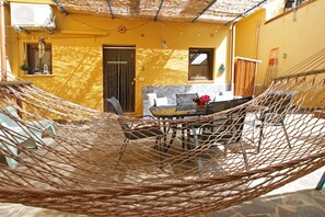 Eine Hängematte in einem sonnendurchfluteten Zimmer mit Esstisch und Stühlen, einem Fenster und einer Tür.