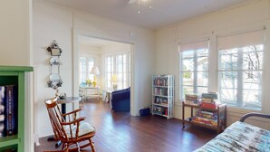 Una habitació espaiosa amb terres de parquets, una cadira bressol de fusta, una biblioteca i una finestra amb vista a arbres.